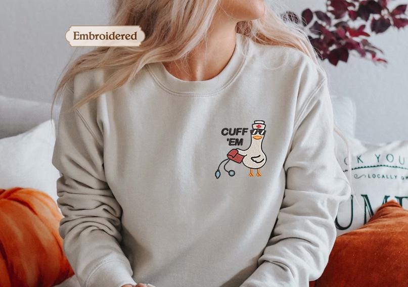 a woman wearing a white sweatshirt with a cartoon duck and the text &quot;Cuff &#39;em&quot; on it.