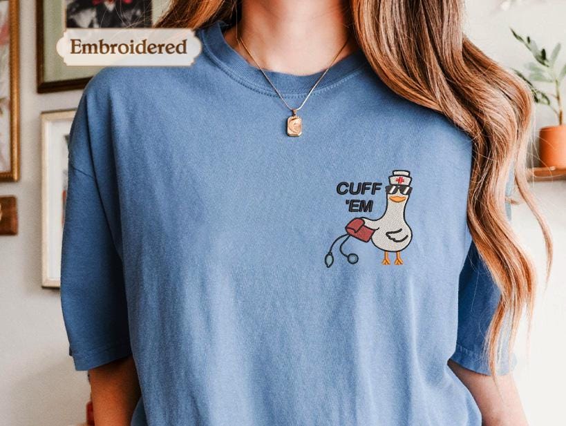 a woman wearing a blue shirt with a cartoon duck and the text &quot;Cuff &#39;em&quot; embroidered on it.