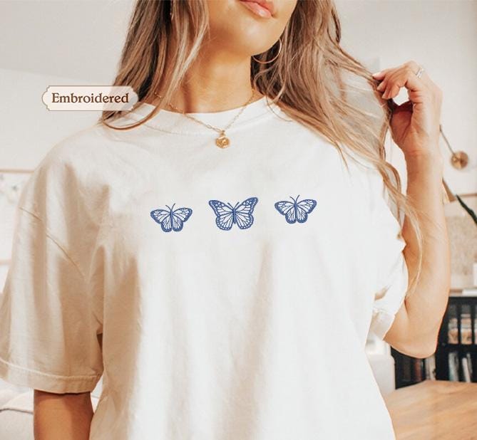a woman wearing a white shirt with blue butterflies on it