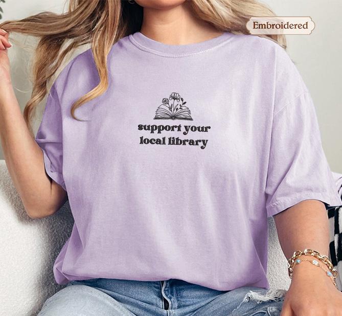 A person wearing a purple t-shirt with the text &quot;Support your local library&quot; printed on it.