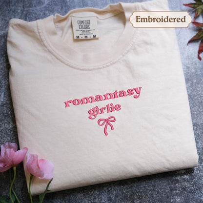A white t-shirt with the text &quot;romantic girl&quot; embroidered on it, along with a bow design.