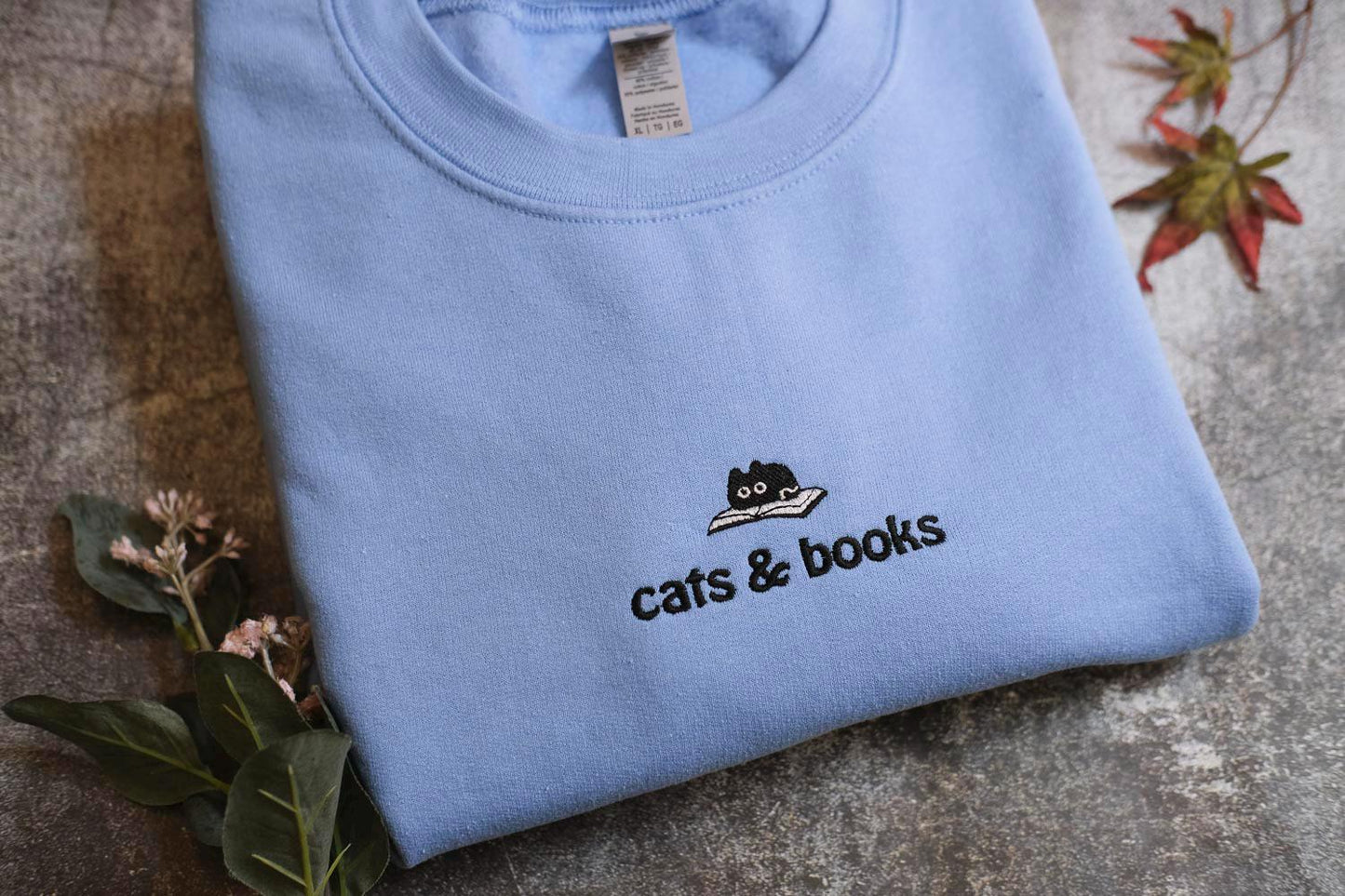 a blue shirt with a cat and books embroidered on it