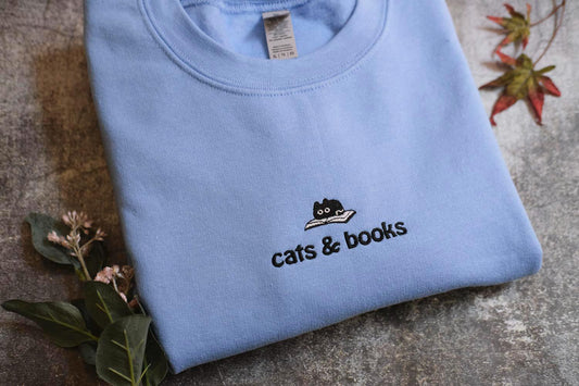 a blue shirt with a cat and books embroidered on it