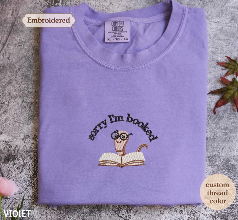 a purple t - shirt with a picture of a cat reading a book