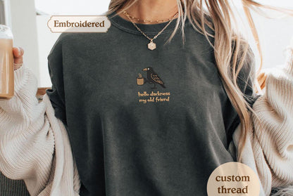 Embroidered shirt with a bird and text on it, wearing a sweater and holding a drink.