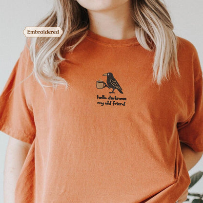 a person wearing an orange t-shirt with a black bird embroidered on it.