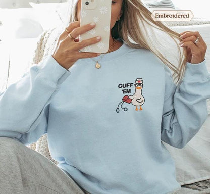a woman taking a selfie with her phone, wearing a light blue sweater with a cartoon duck on it.