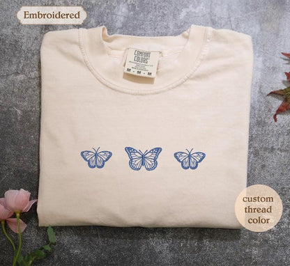 a white t - shirt with three blue butterflies on it