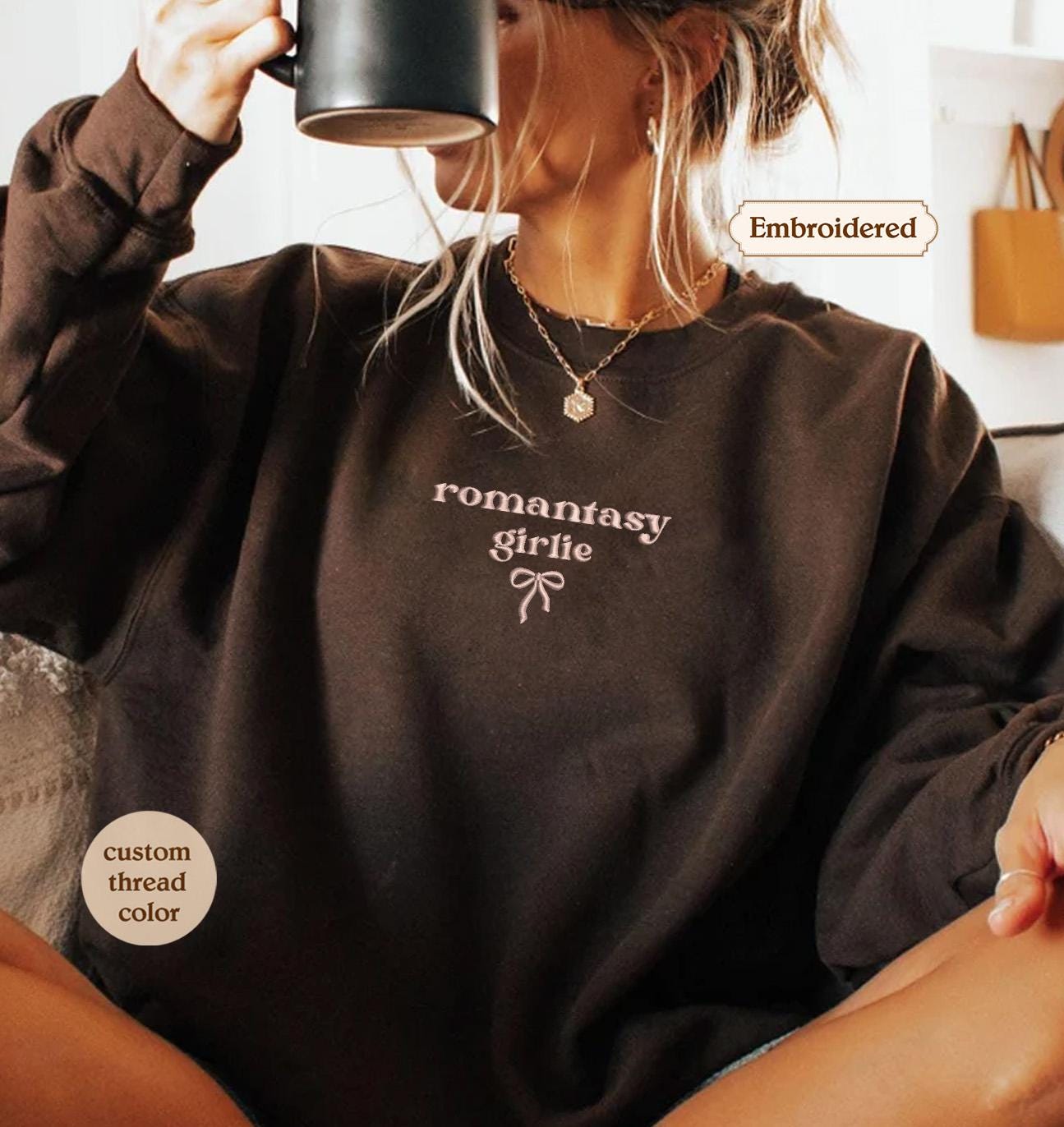 A woman wearing a brown sweater with the text &quot;romantic girl&quot; printed on it, sitting and drinking from a mug.