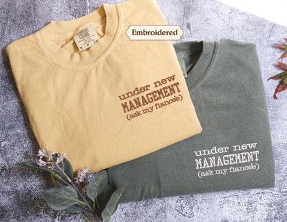 two t-shirts with humorous text printed on them, one in a light yellow color and the other in a dark green color.